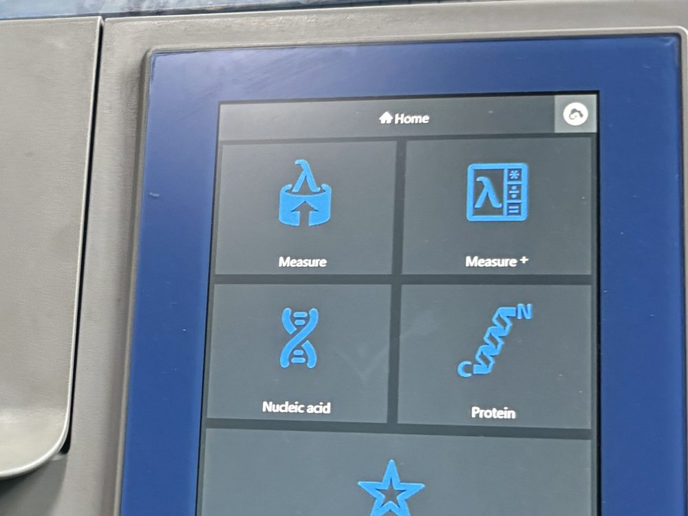 A benchtop spectrophotometer with its menu screen lit and a cover resting on top.